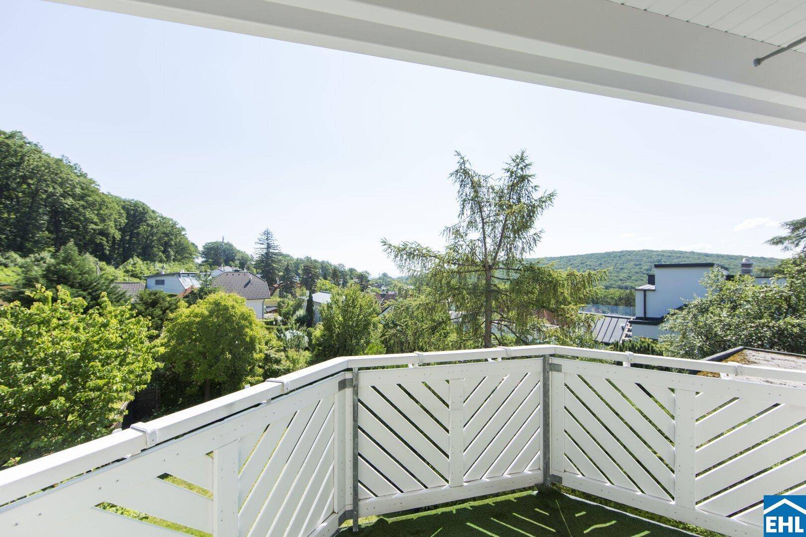 Sonniger Balkon mit weißem Geländer und weitem Blick über grüne Hügel und Dächer.