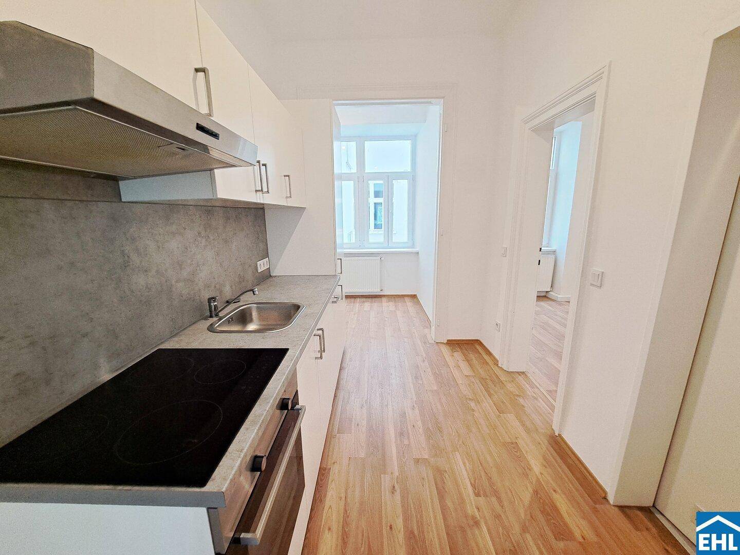 Moderne Küche mit weißen Schränken, Induktionskochfeld und Laminatboden, hell beleuchtet.