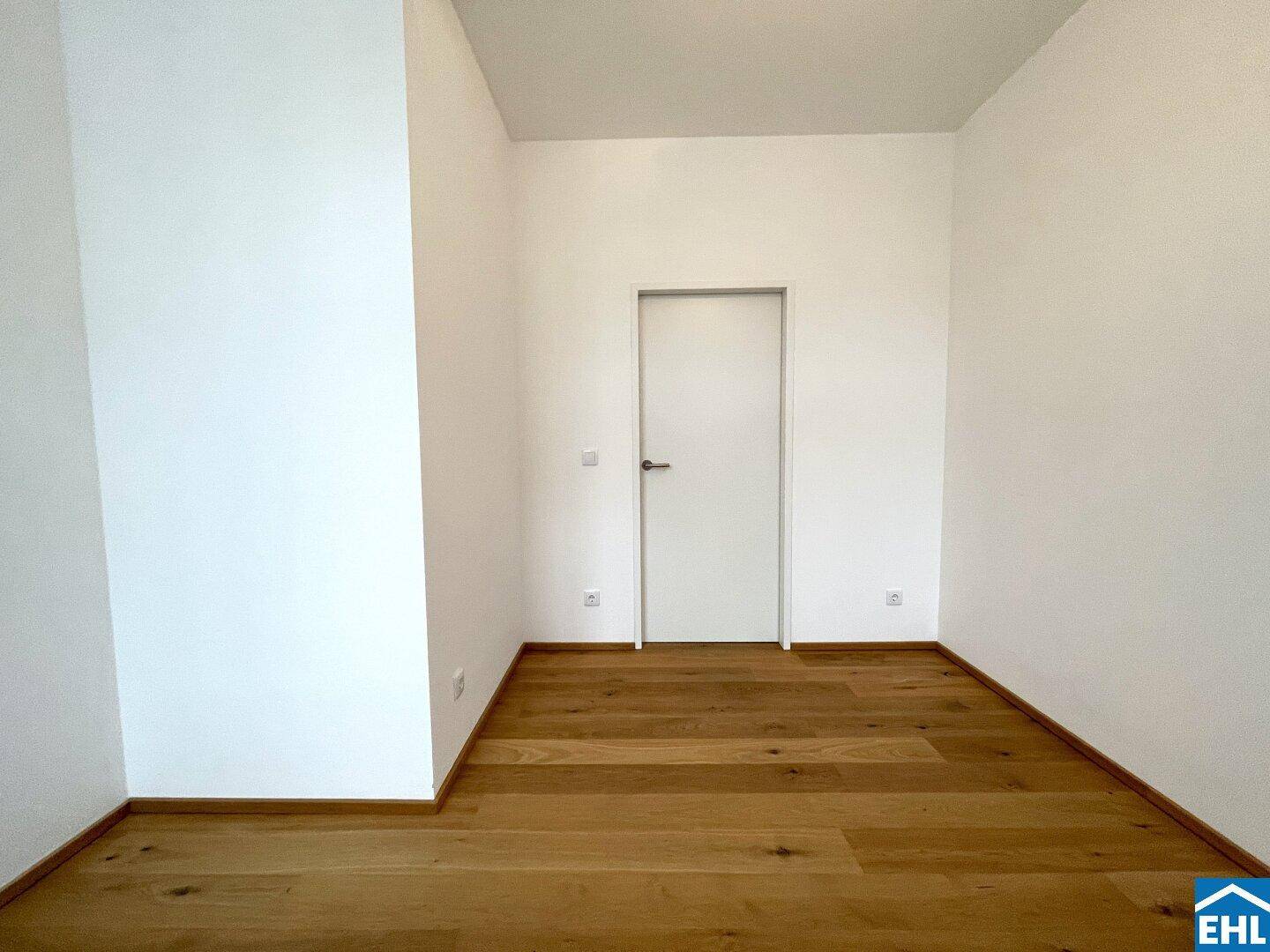 Leerer Raum mit Holzboden und einer modernen weißen Tür, bereit zur individuellen Gestaltung.