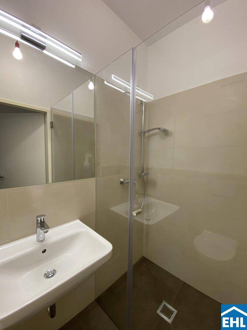 Modernes Badezimmer mit begehbarer Dusche, Einzelwaschbecken und hellen Fliesen.