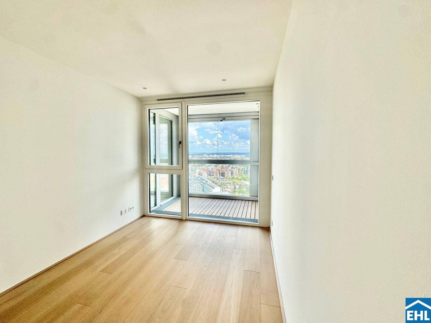 Helles Schlafzimmer mit Holzparkett und Zugang zu einem kleinen Balkon mit Aussicht.