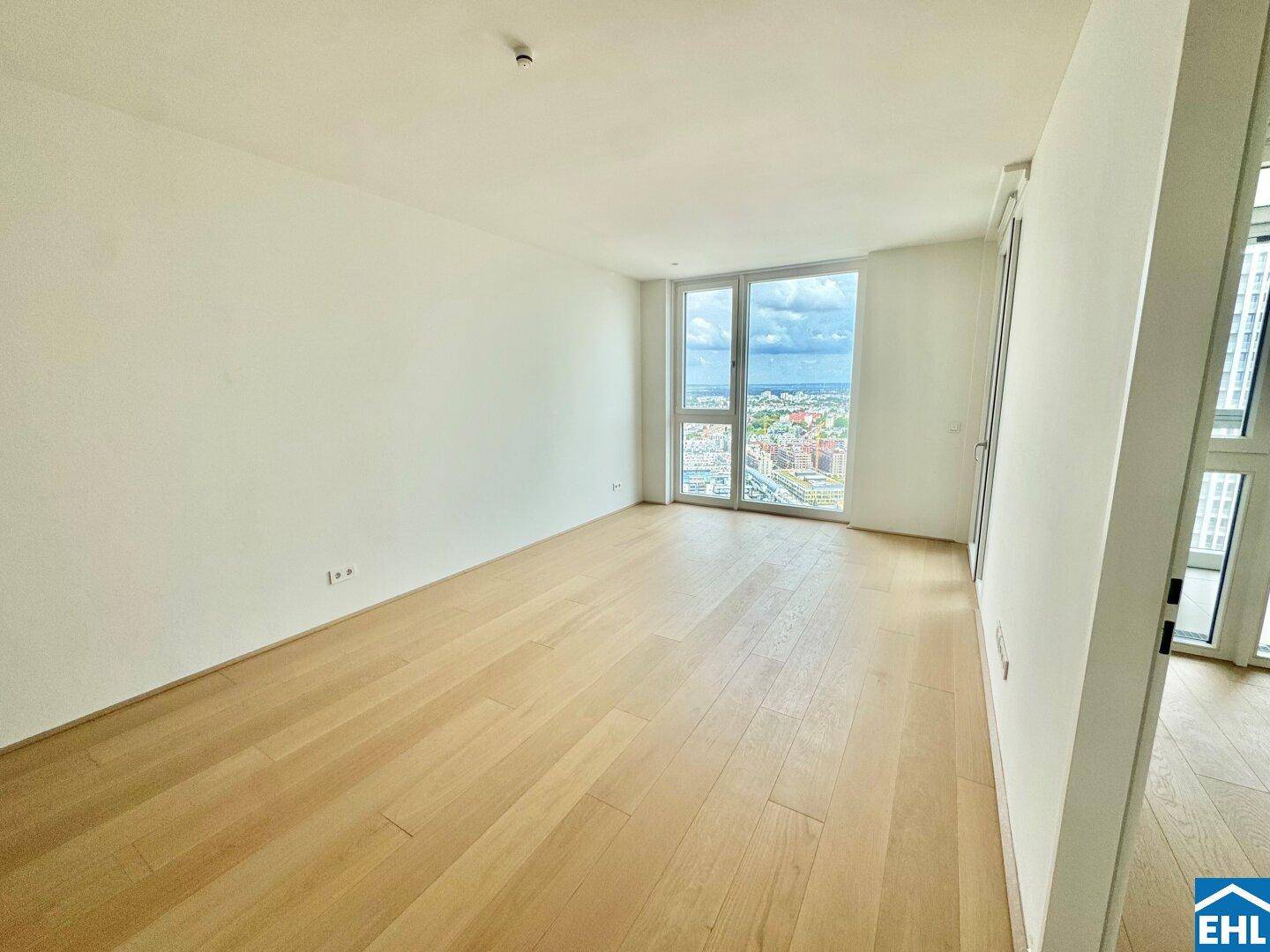 Geräumiger, heller Wohnraum mit Holzparkett und großen Fenstern, bereit zur Einrichtung.