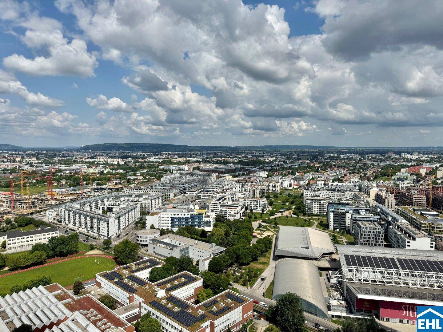 Weitläufiger Blick über die Stadt mit modernen Wohngebäuden und Grünflächen unter blauem Himmel.