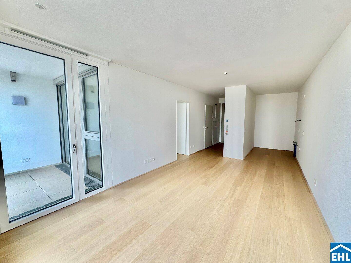 Geräumiges, helles Zimmer mit Holzboden und großen Fenstern, ideal für offenes Wohnen.