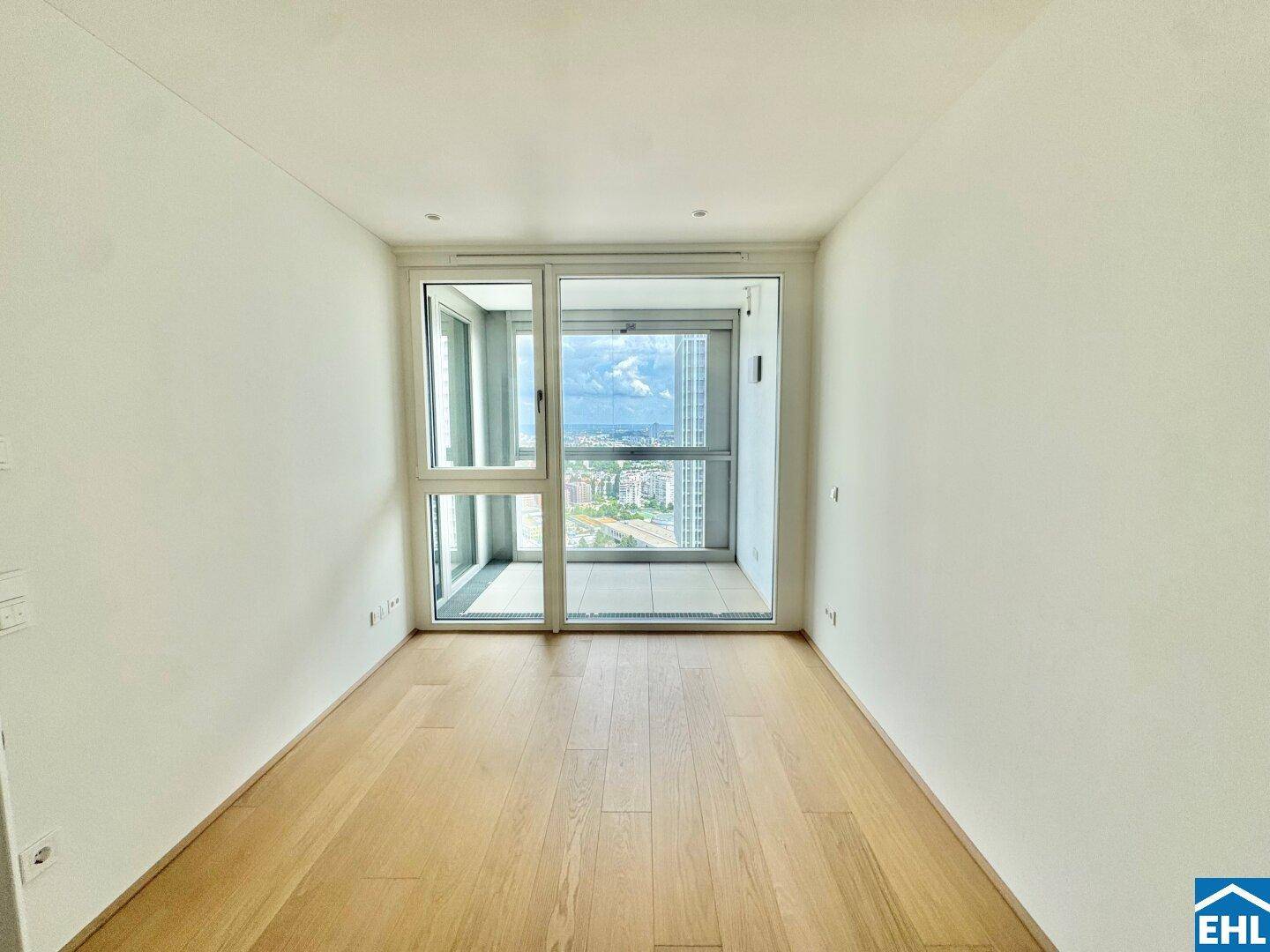 Helles Schlafzimmer mit Holzboden und Zugang zu einem Balkon mit Panoramablick über die Stadt.