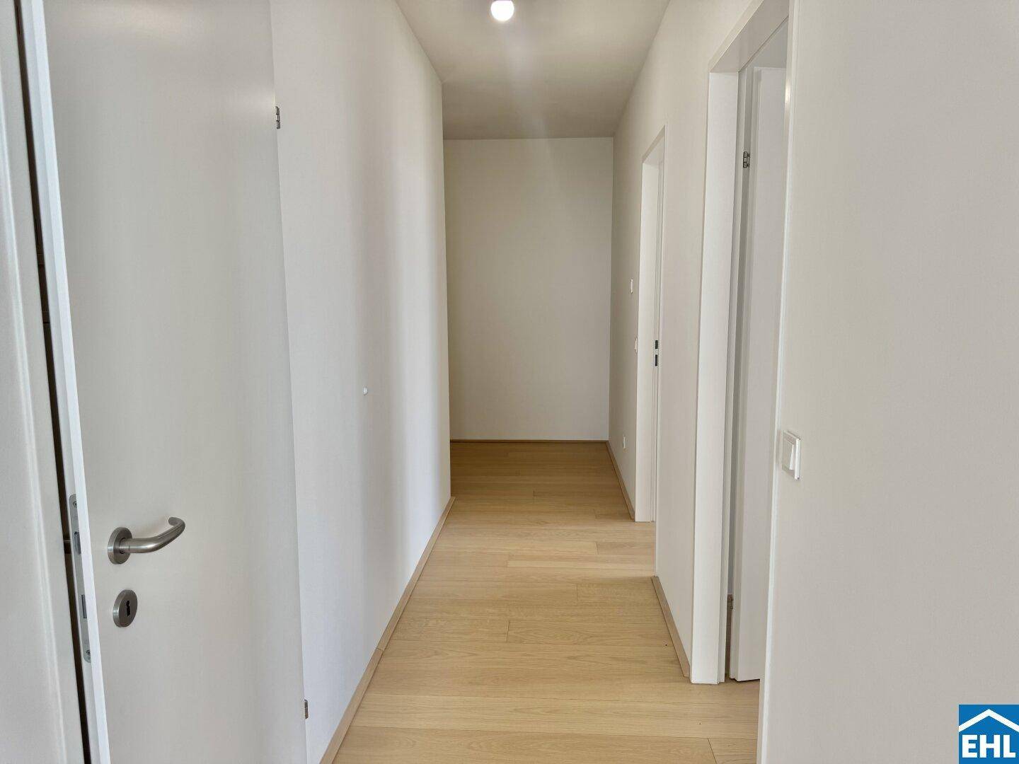 Heller Flur mit Holzboden und weißen Wänden, der zu weiteren Räumen führt.