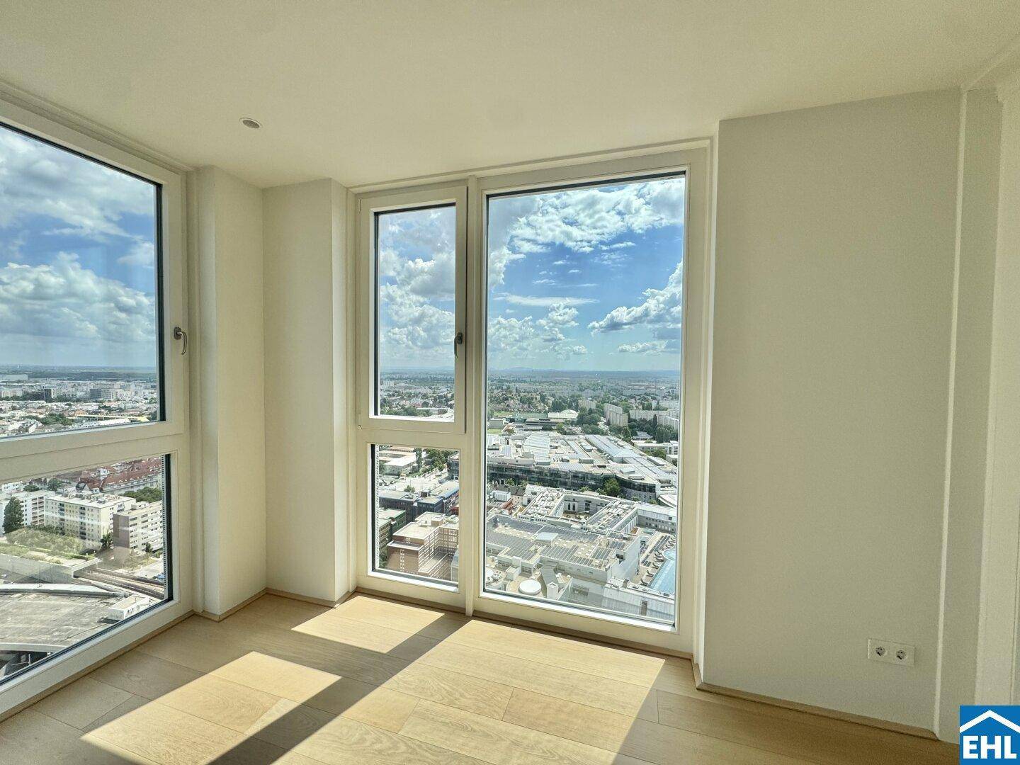 Lichtdurchfluteter Raum mit Holzboden und Panoramafenstern, die eine beeindruckende Aussicht auf die Stadt ermöglichen.