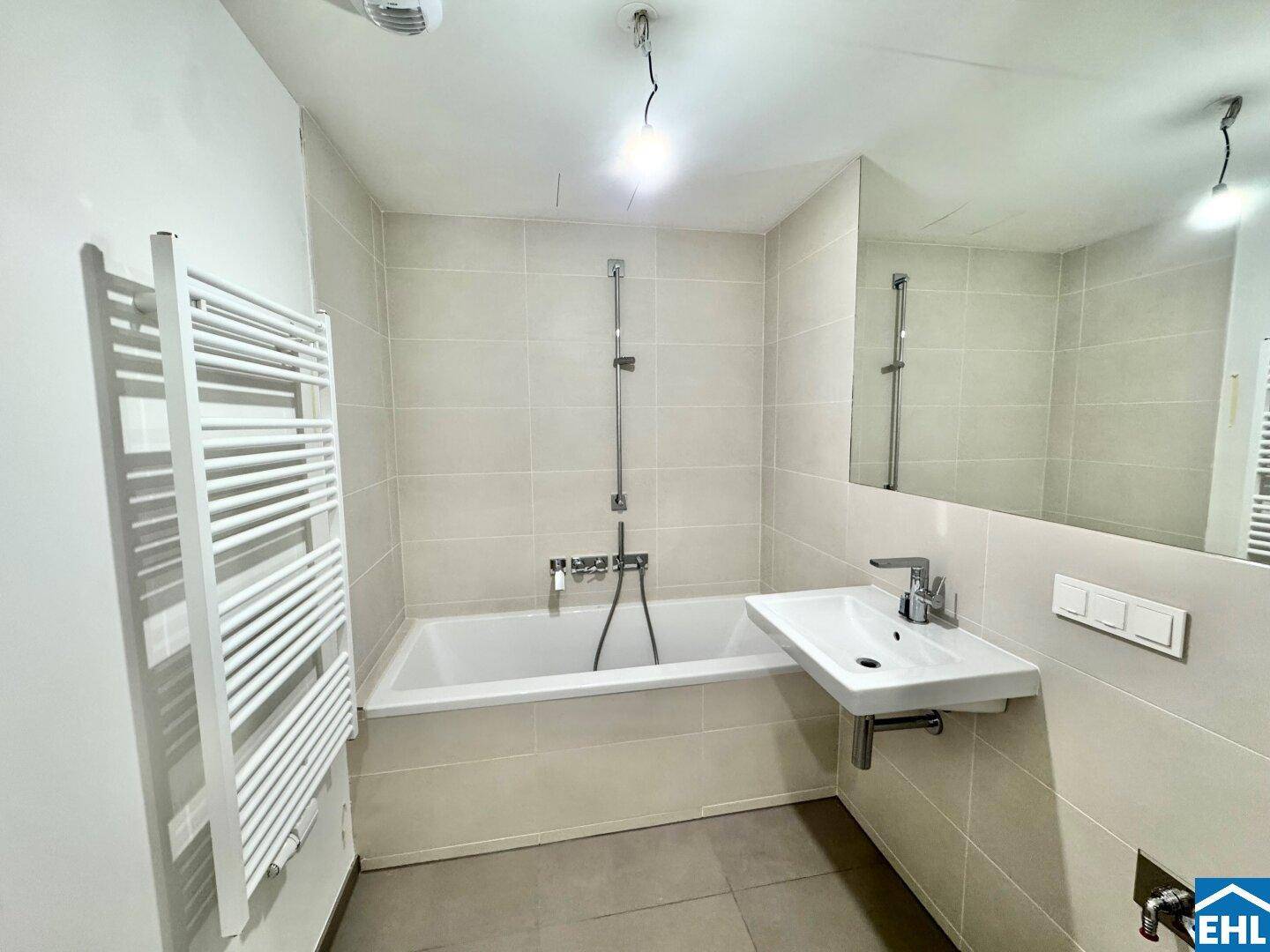 Modernes Badezimmer mit Badewanne, Einzelwaschbecken und beheiztem Handtuchhalter in hellen Fliesen.