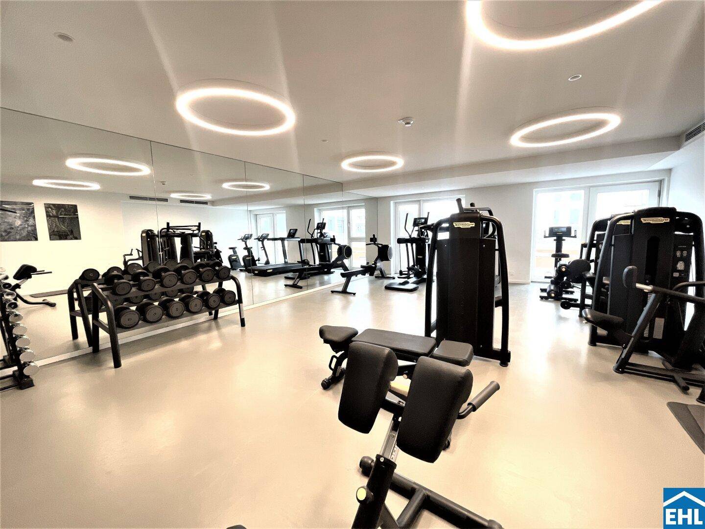 Geräumiger Fitnessraum mit modernen Trainingsgeräten und großen Spiegeln.