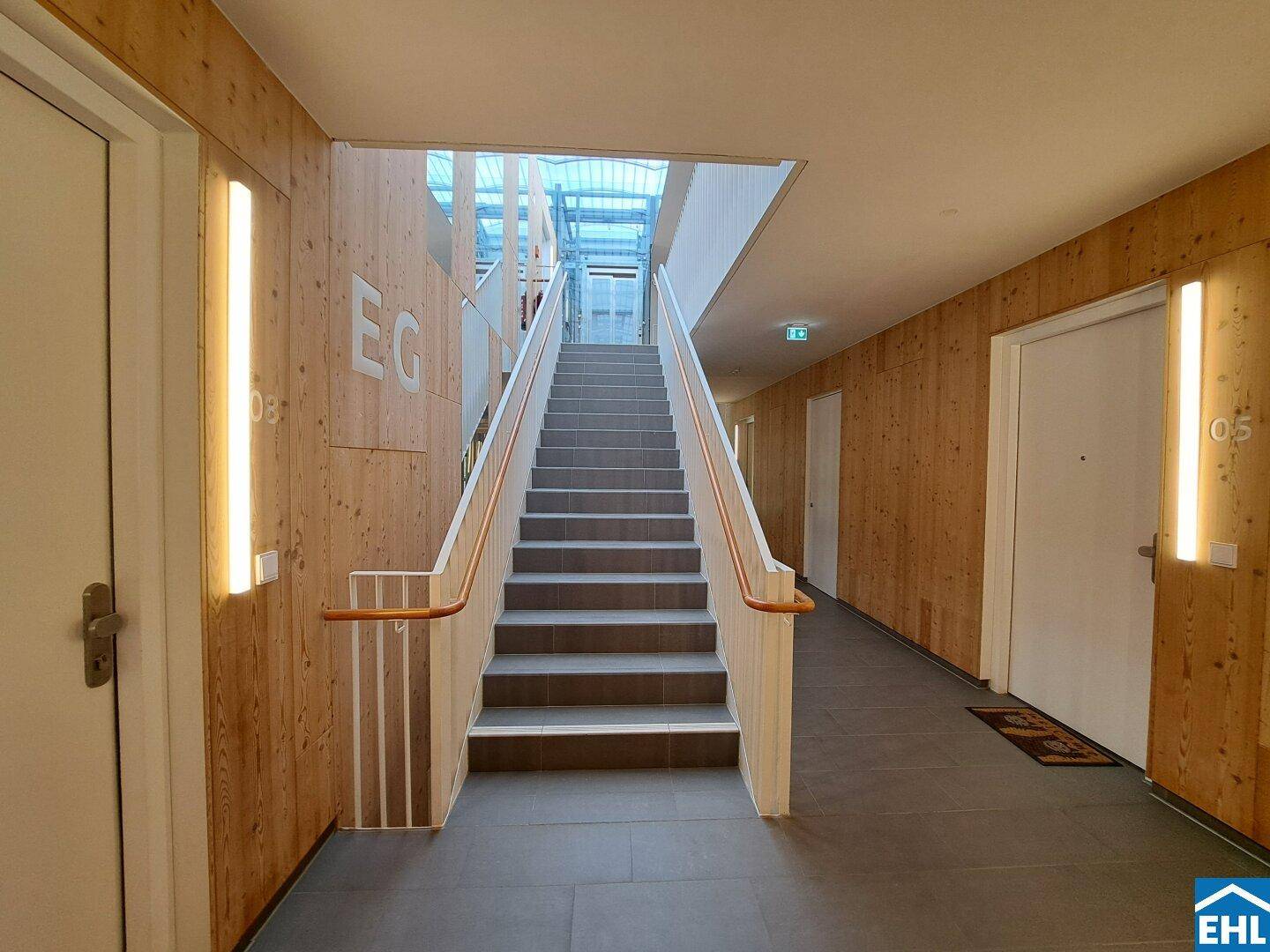 Heller Treppenaufgang mit Holzverkleidung und modernen Leuchten, verbindet die Stockwerke des Gebäudes.