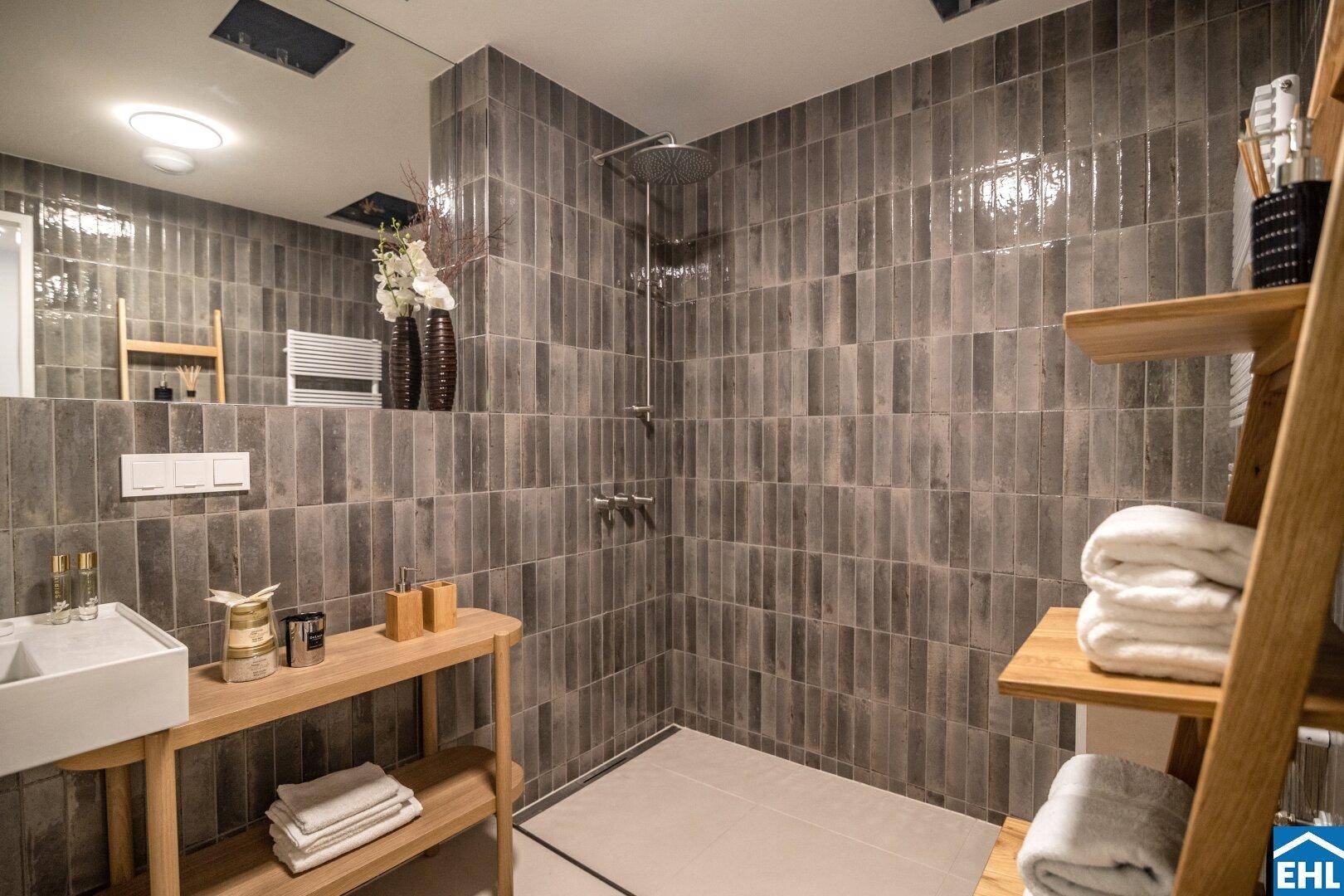 Modernes Badezimmer mit grauen Fliesen, begehbarer Dusche und Holzregalen.