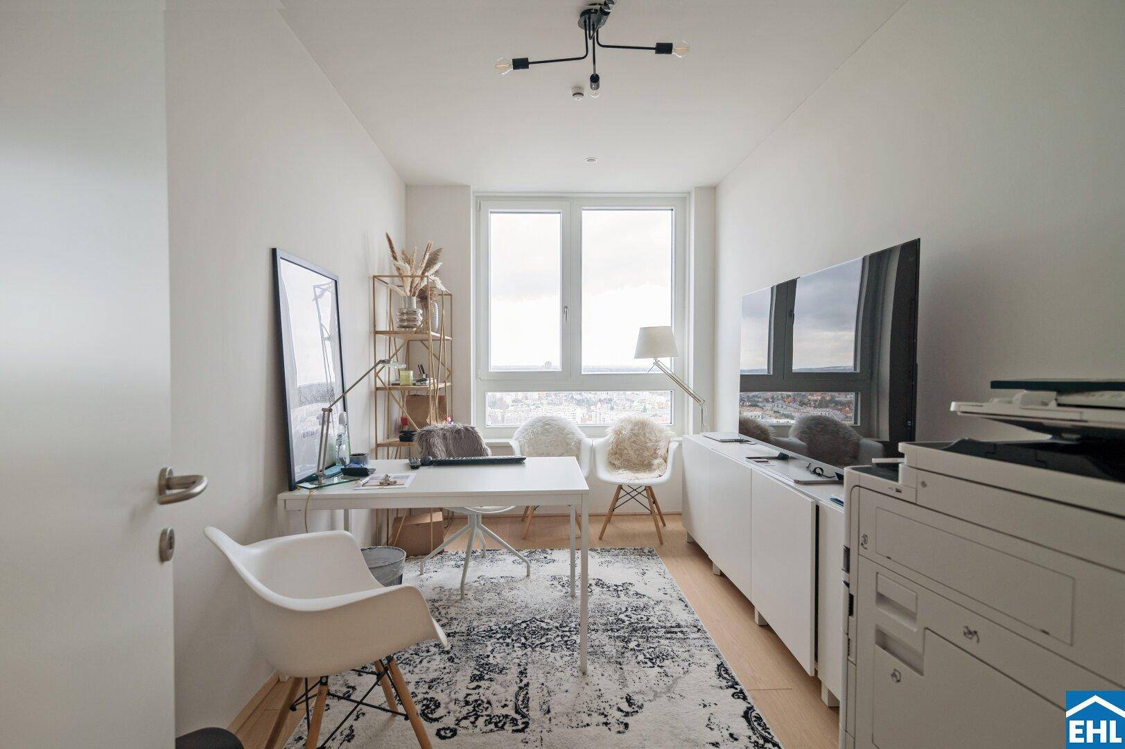 Helles Arbeitszimmer mit Schreibtisch, Regal und großem Fenster, das einen weiten Blick bietet.