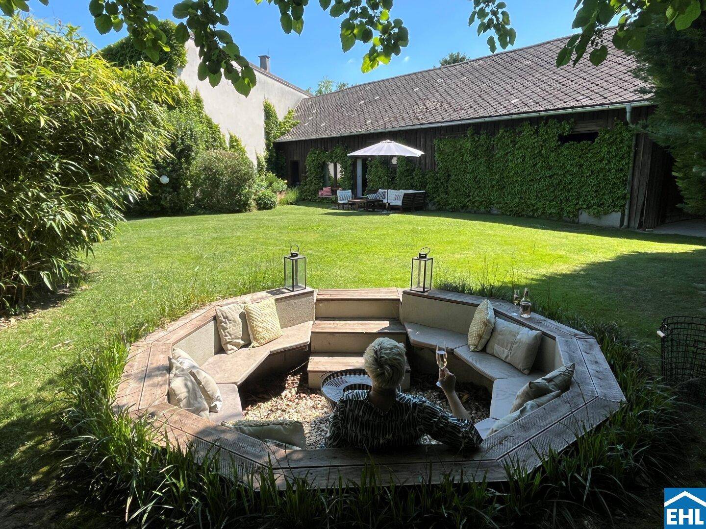 Gemütliche Feuerstelle im Garten mit integrierten Sitzgelegenheiten und Blick auf das begrünte Gebäude.