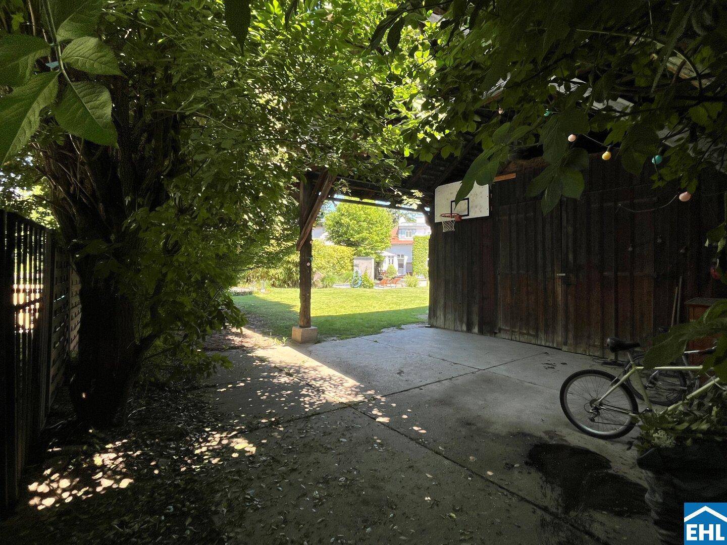 Überdachter Außenbereich mit Basketballkorb und Fahrrad, bietet Schutz und Zugang zum grünen Garten.