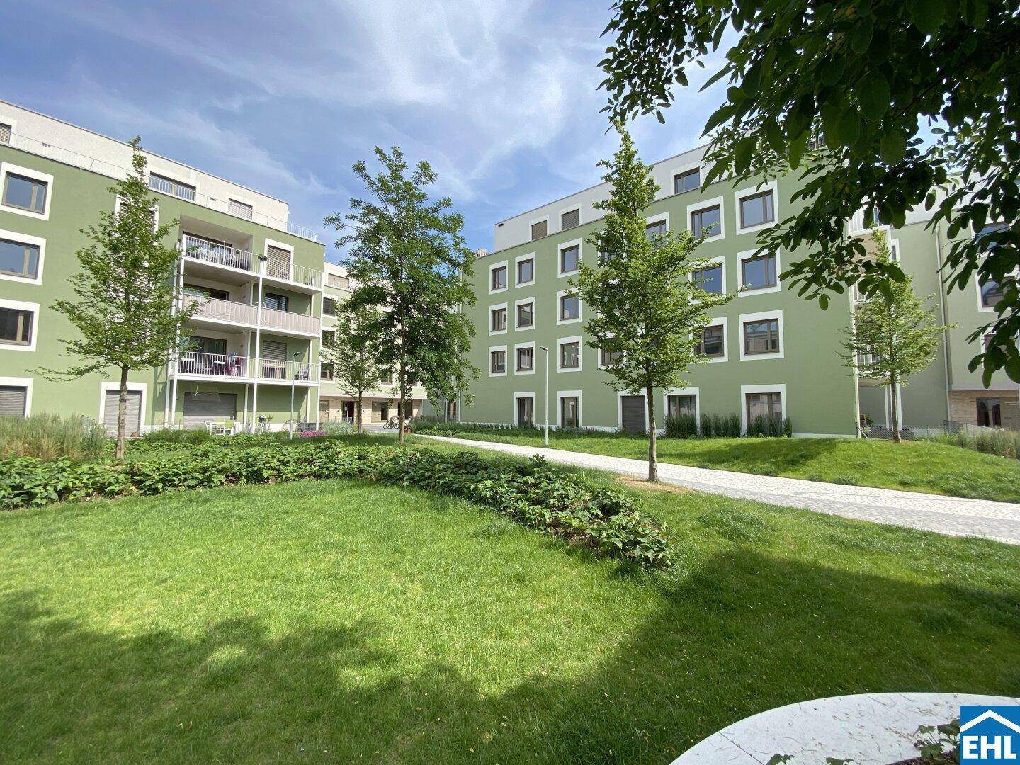 Grüne Außenanlage mit jungen Bäumen und gepflegten Rasenflächen zwischen modernen Wohngebäuden.
