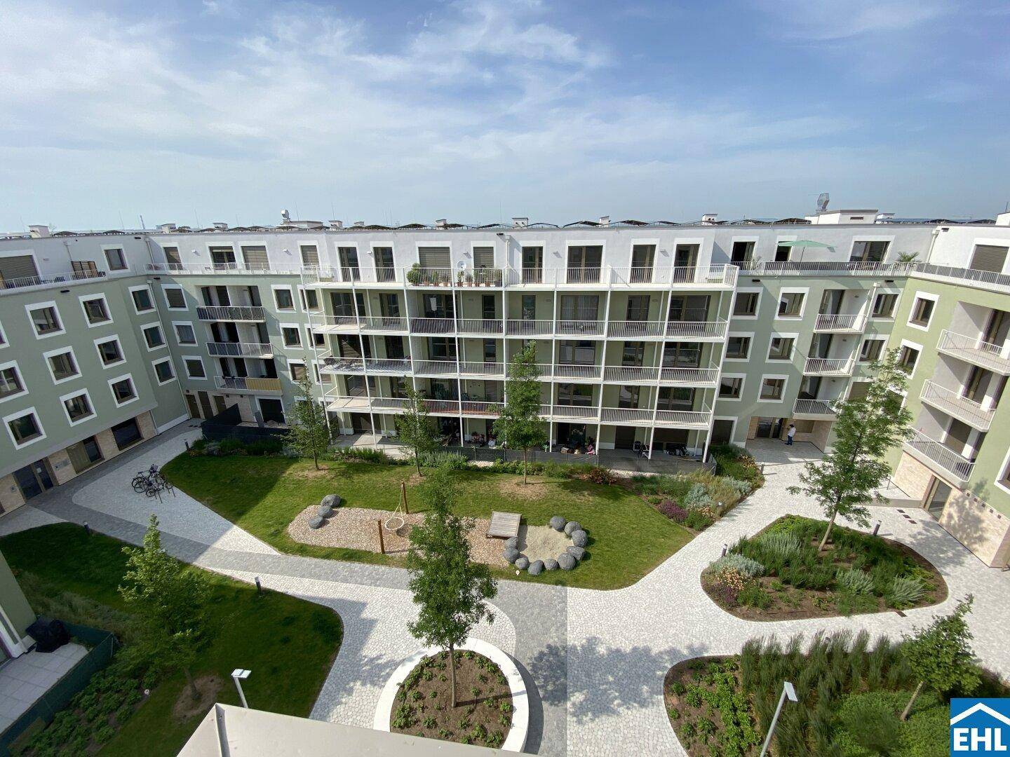Innenhof einer Wohnanlage mit Spielplatz, Sitzgelegenheiten und begrünten Inseln, umgeben von Balkonen.