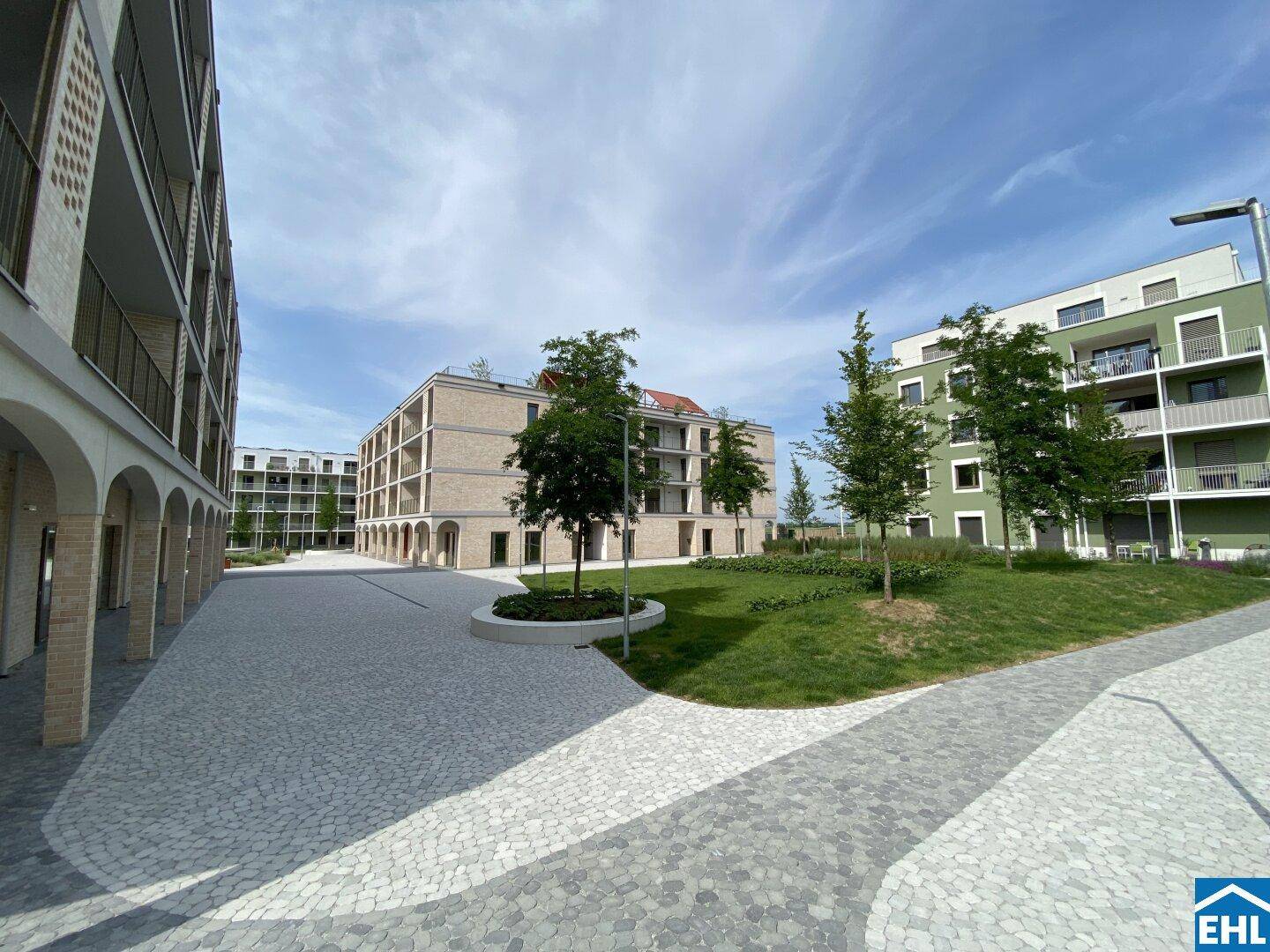 Moderne Wohngebäude mit ansprechenden Fassaden und gepflasterten Wegen in einer weitläufigen Anlage.