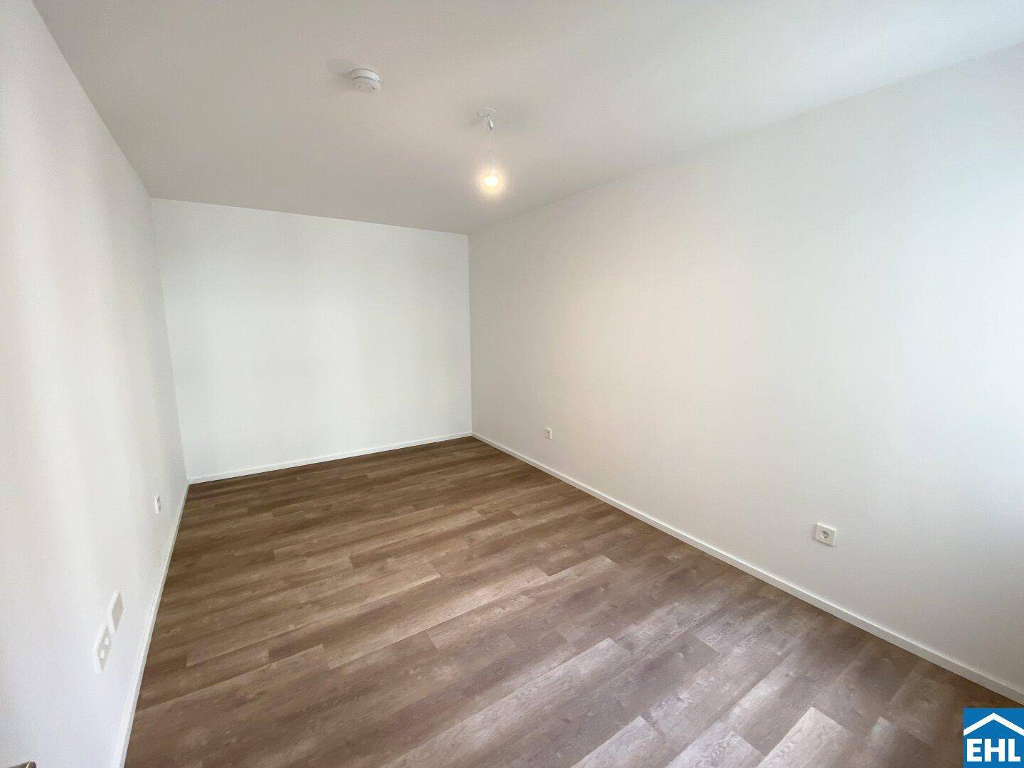 Leeres Schlafzimmer mit hellem Laminatboden und weißen Wänden, bereit zur individuellen Gestaltung.