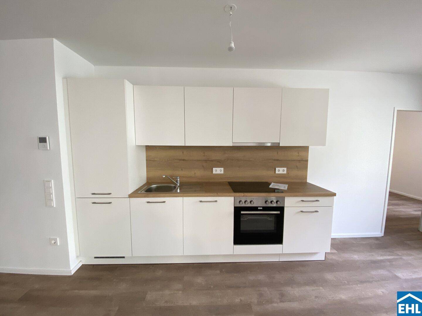 Moderne Einbauküche mit weißen Fronten, Holzoptik-Arbeitsplatte und integrierten Geräten.