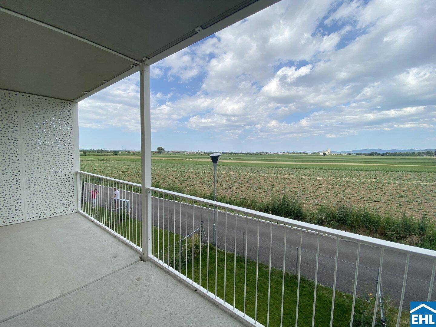 Geräumiger Balkon mit weitem Blick über grüne Felder und die umliegende Landschaft unter bewölktem Himmel.
