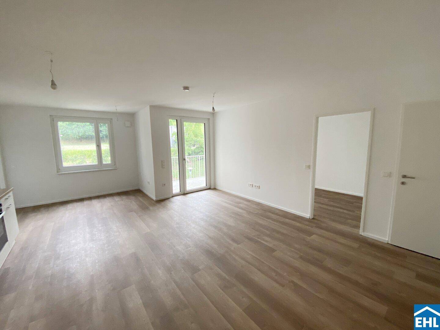 Helles, offenes Wohnzimmer mit modernem Laminatboden und Zugang zu einem Balkon.