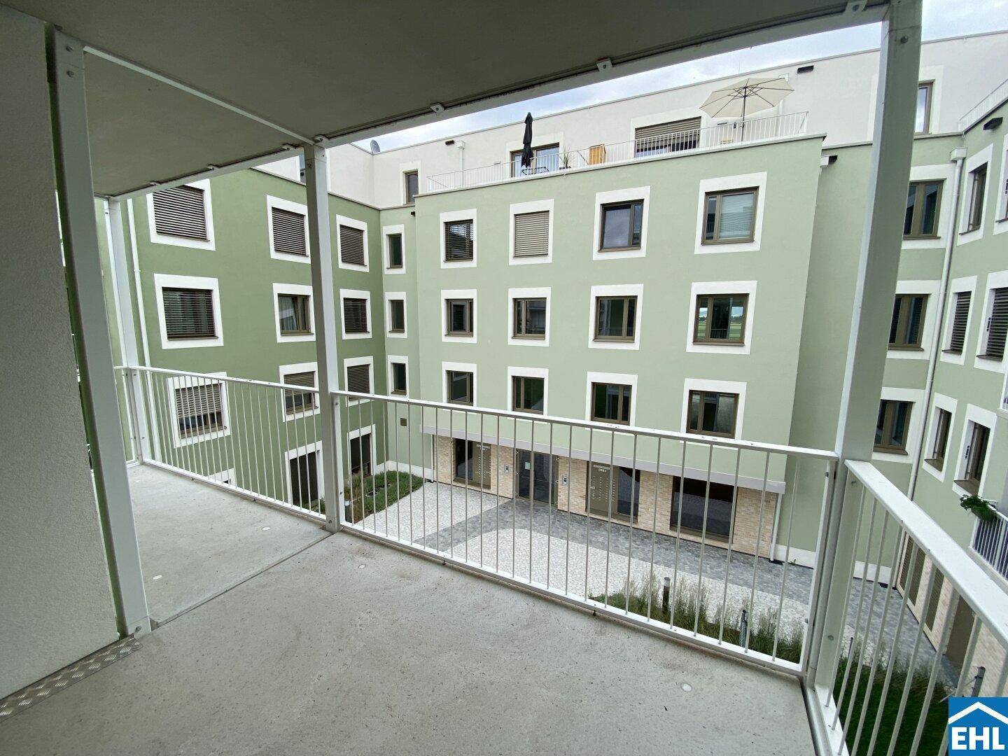 Balkon mit Blick auf den begrünten Innenhof und die moderne Gebäudefassade.