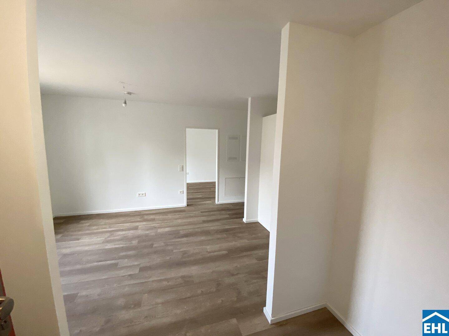 Offener Wohnbereich mit hellem Vinylboden und weiß gestrichenen Wänden, bereit zum Einzug.
