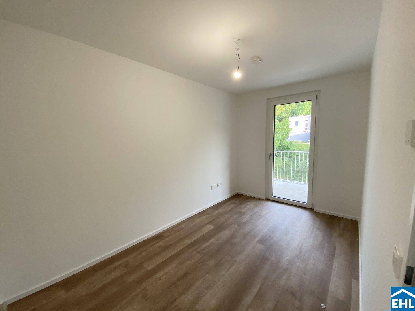 Schlafzimmer mit Balkonzugang, modernem Vinylboden und viel Tageslicht.