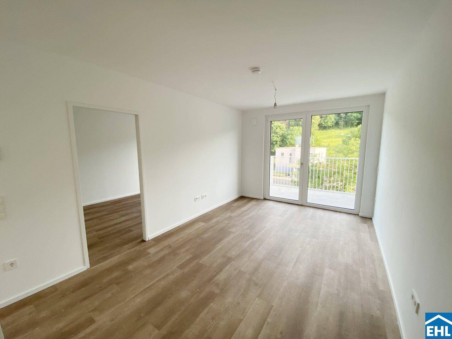 Heller Wohnbereich mit Laminatboden, großen Fenstern und Zugang zum Balkon.