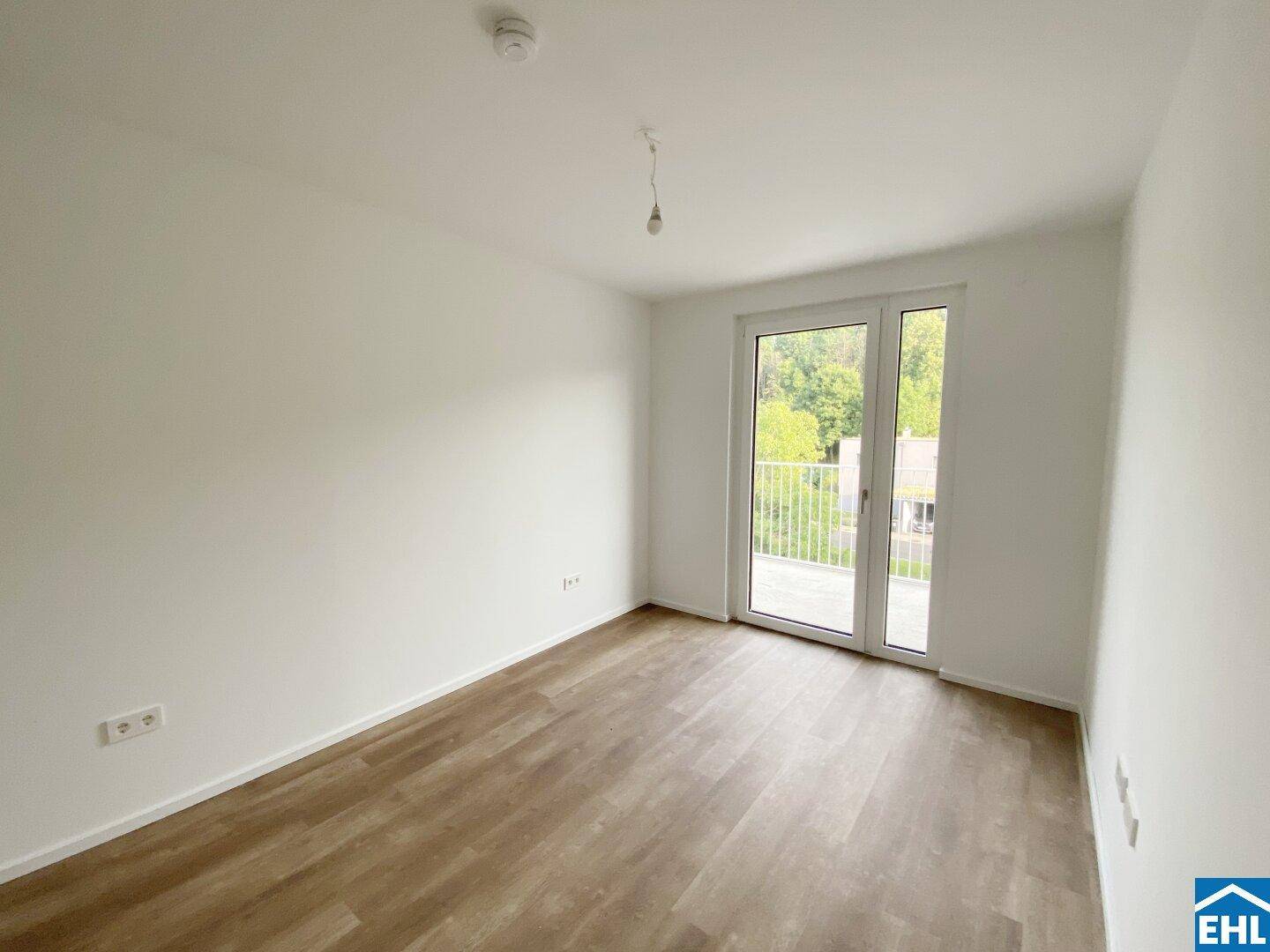 Helles Zimmer mit Balkonzugang und Laminatboden, bietet einen grünen Ausblick.