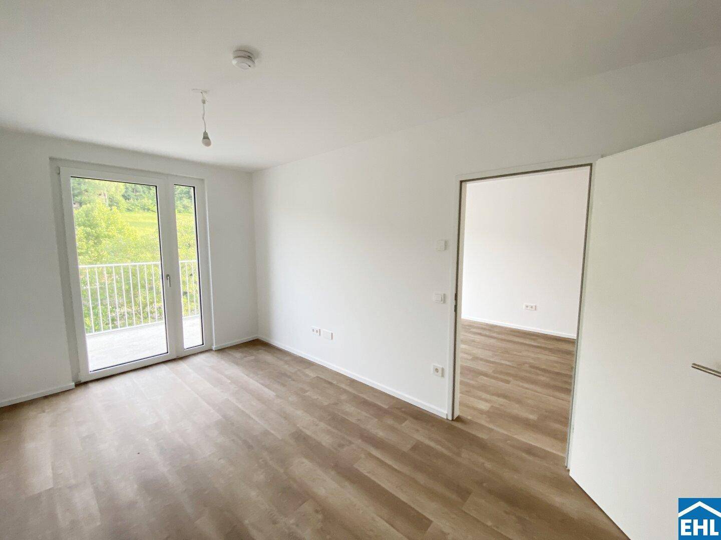 Geräumiges Zimmer mit Laminatboden und Zugang zu einem weiteren Raum sowie Balkon.