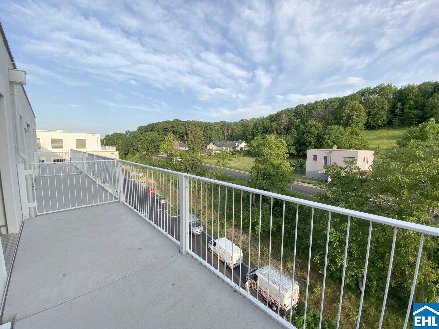 Langer Balkon mit Metallgeländer und Blick auf die Straße und bewaldete Hügel.