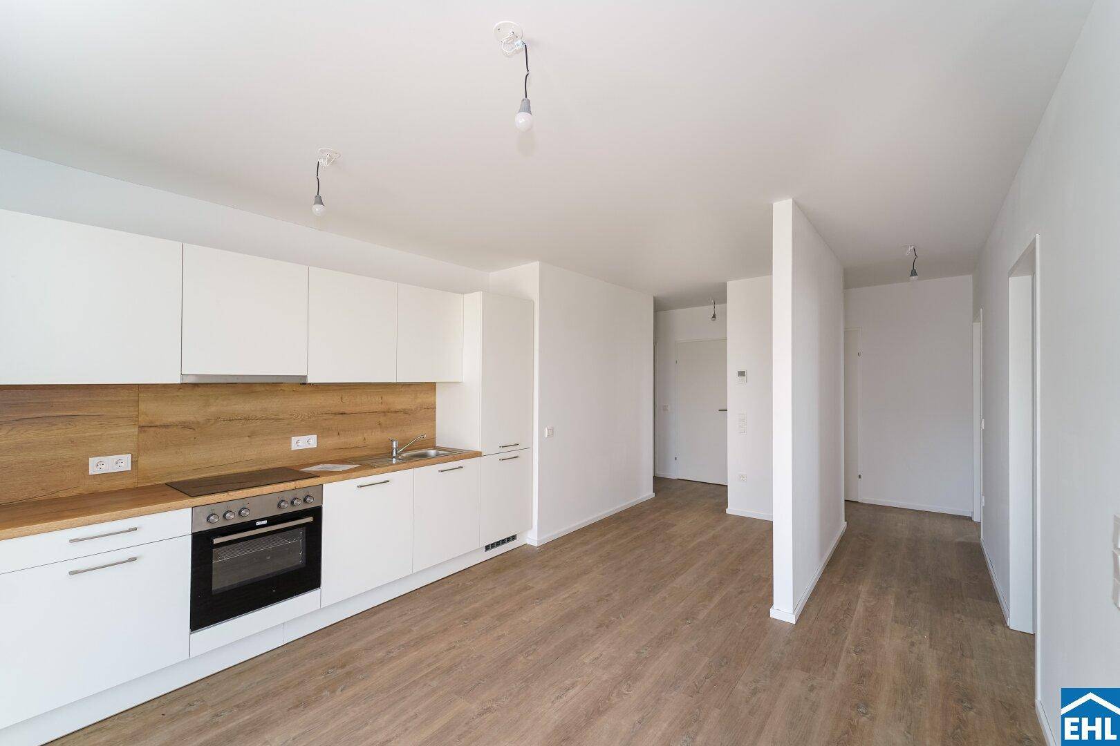 Moderne Einbauküche mit weißen Schränken, Holzarbeitsplatte und integrierten Geräten in offenem Raum.