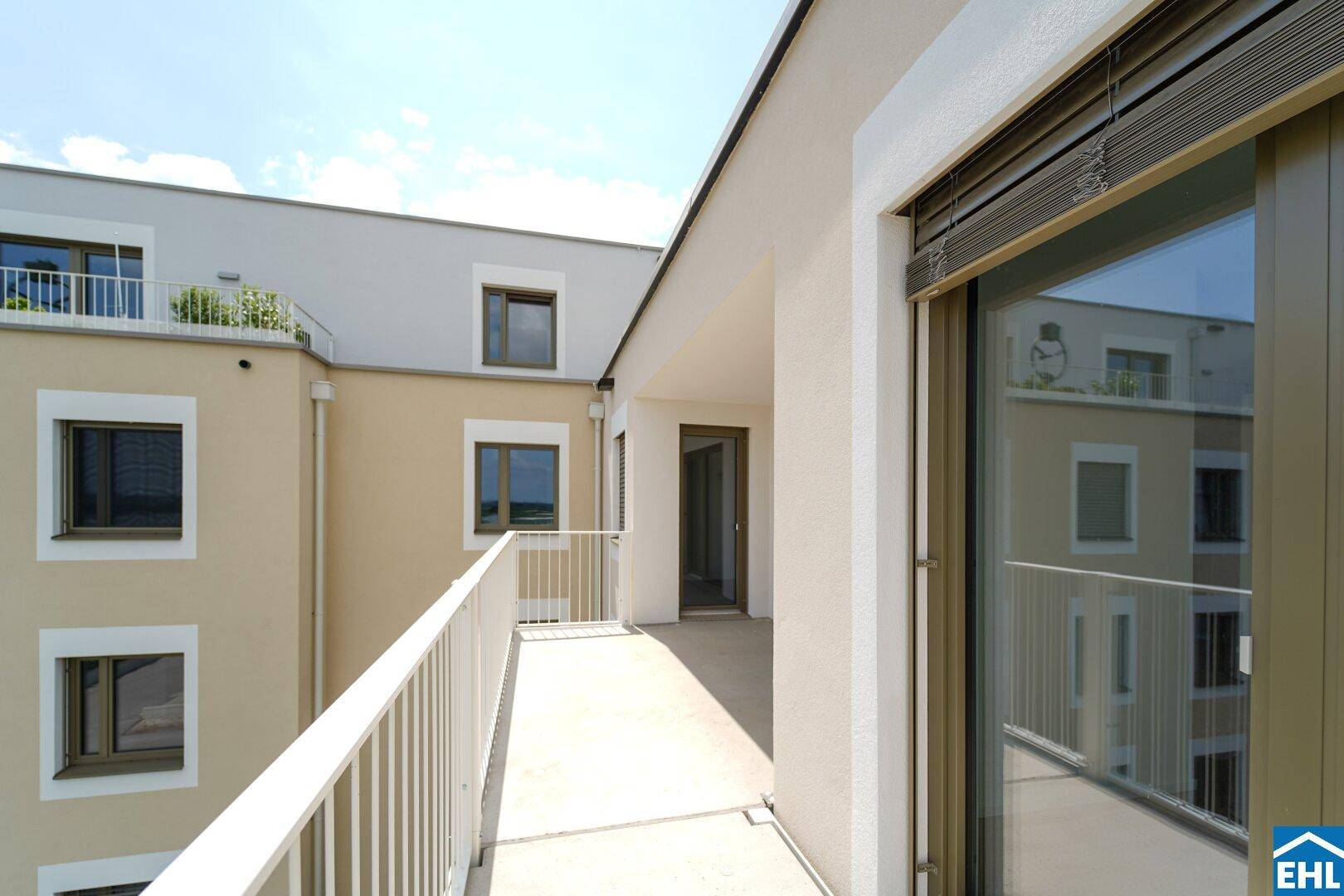 Langer Balkon entlang der Gebäudefassade mit Blick auf den Innenhof und weitere Wohnungen.