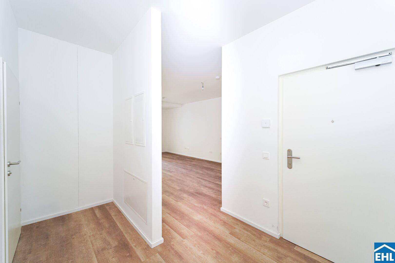 Heller Eingangsbereich mit weiß gestrichenen Wänden und modernem Vinylboden, der in weitere Räume führt.