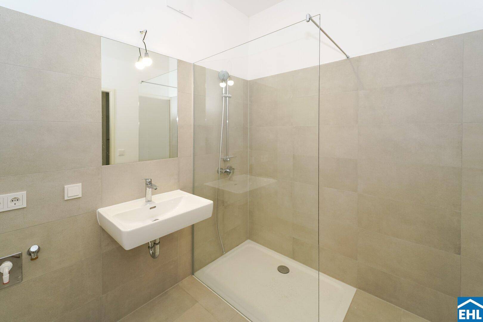 Modernes Badezimmer mit beigefarbenen Fliesen, wandhängendem Waschbecken und einer begehbaren Dusche.