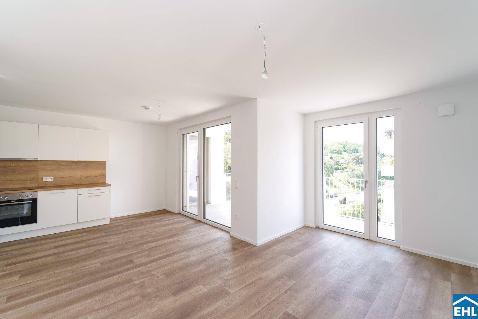Lichtdurchfluteter Wohnbereich mit zwei großen Schiebetüren, die zu einem Balkon führen.