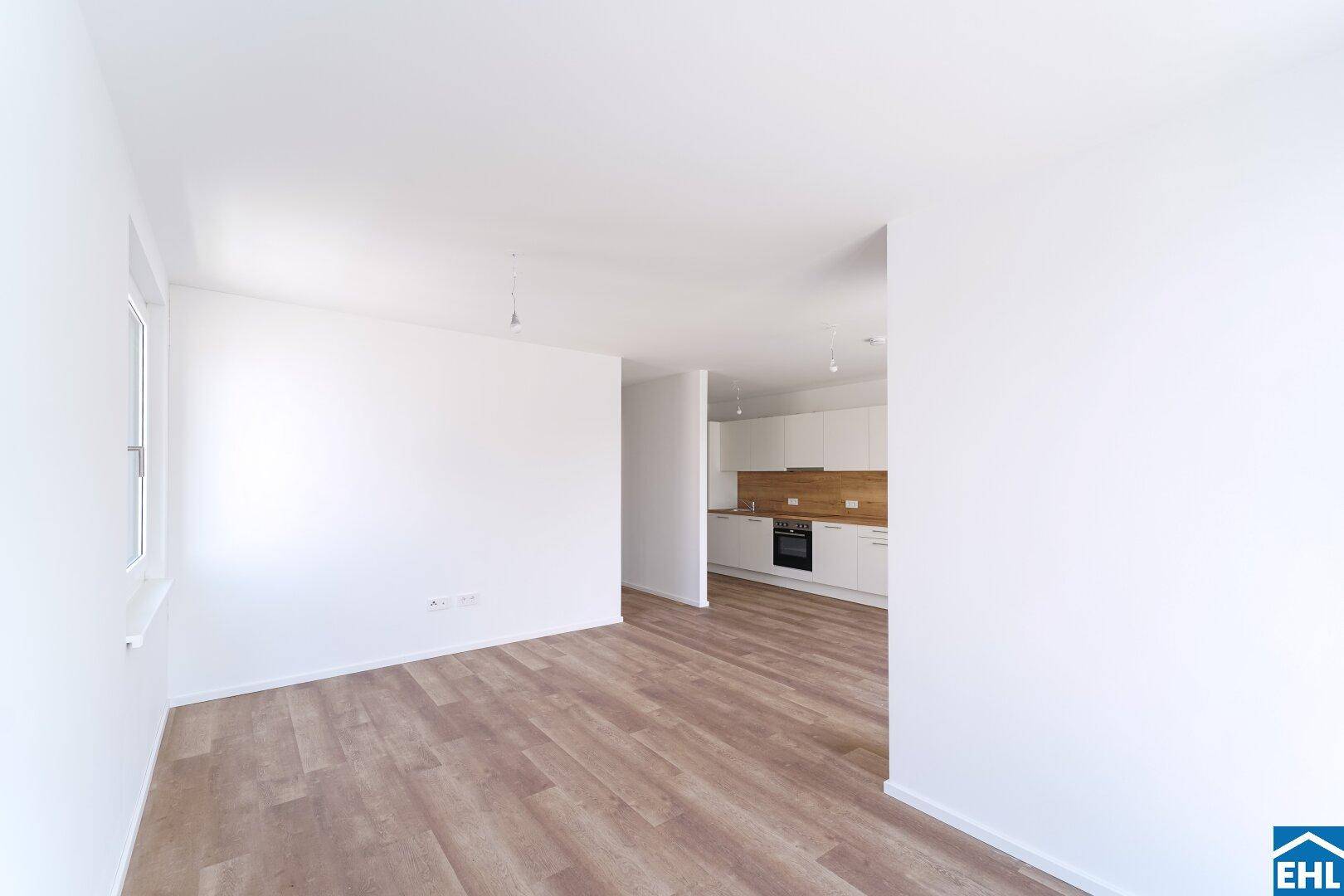 Geräumiger, heller Wohnbereich mit Blick auf die moderne Einbauküche und Laminatboden.