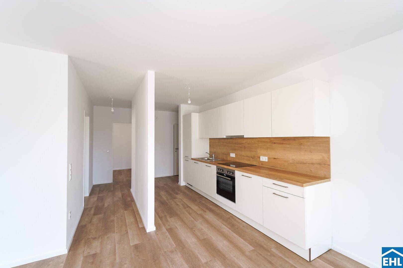 Moderne Einbauküche mit weißen Schränken und Holzoptik-Arbeitsplatte in einem hellen, offenen Bereich.
