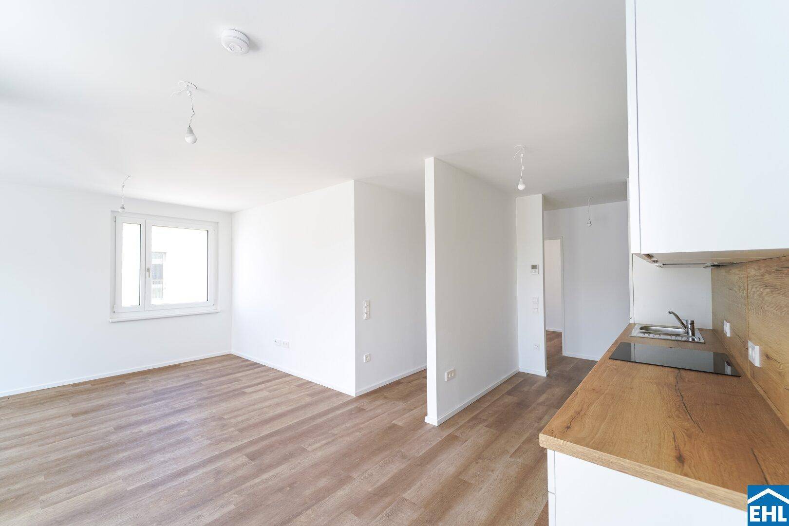 Heller, offener Wohnbereich mit großem Fenster und neuem Laminatboden, angrenzend an die Küche.