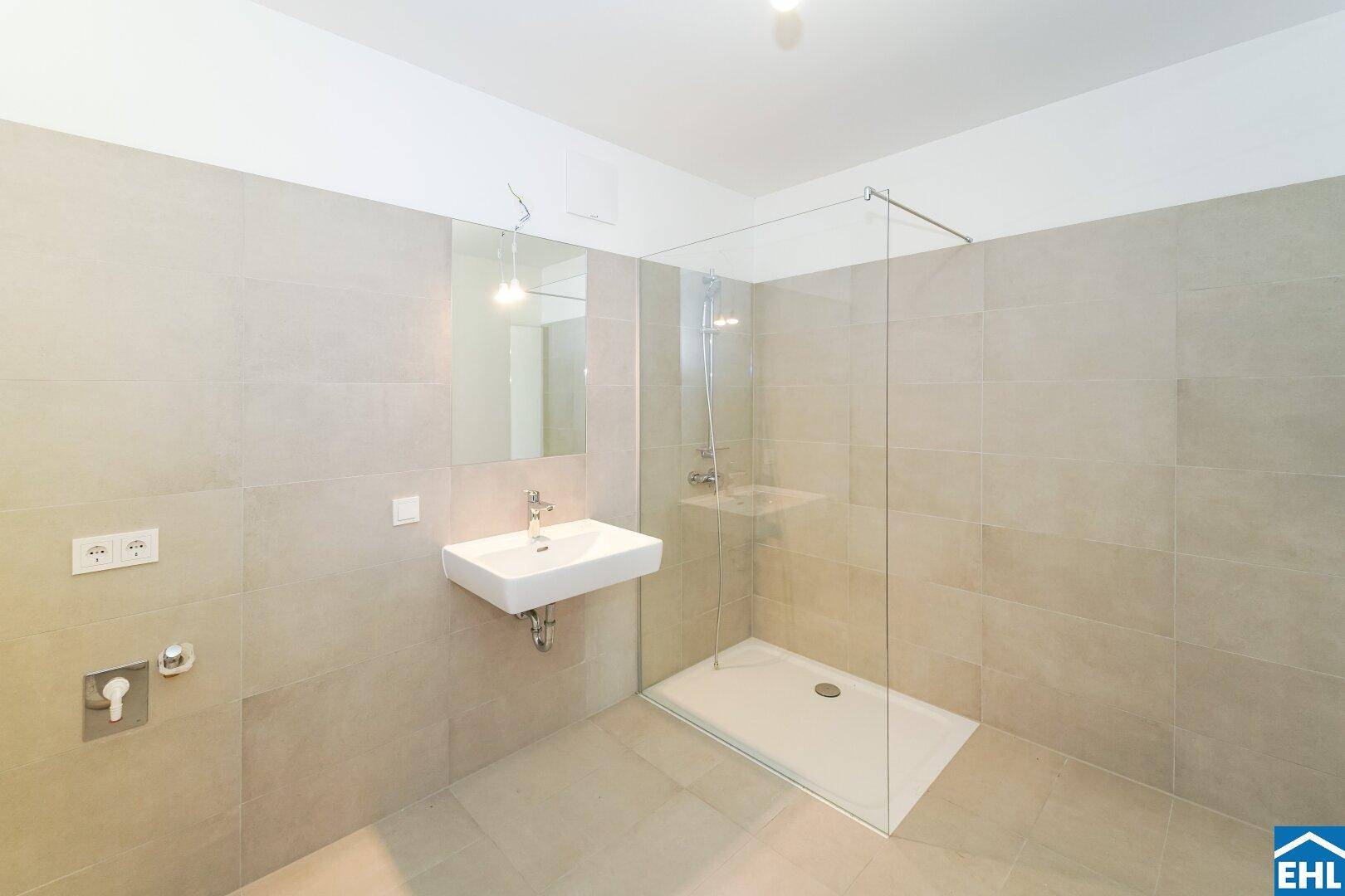 Modernes Badezimmer mit großen hellgrauen Fliesen, wandhängendem Waschbecken und begehbarer Dusche.