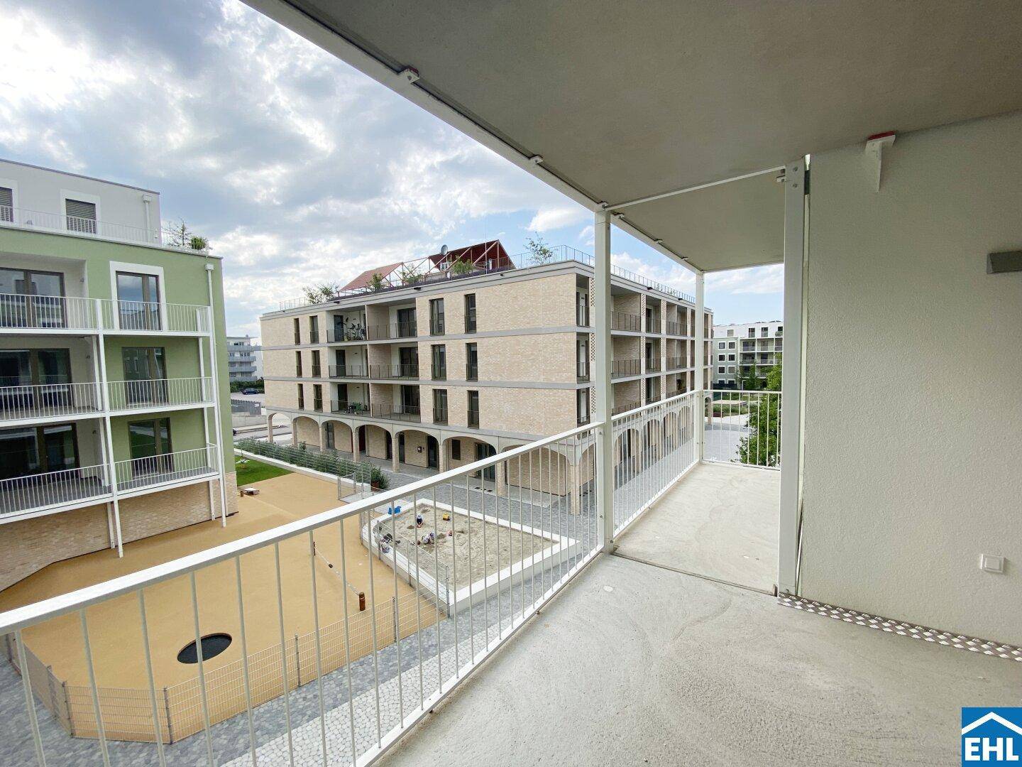 Balkon mit Ausblick auf einen modernen Innenhof mit Spielplatz und Wohngebäuden.