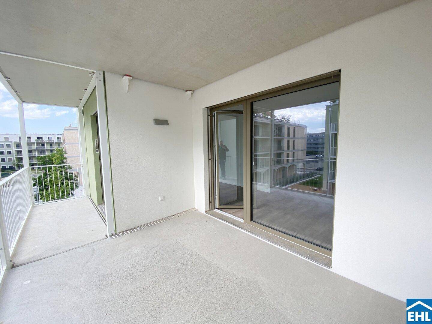 Heller Balkon mit großer Glasfront, die den Zugang zum Innenbereich ermöglicht und Ausblick bietet.