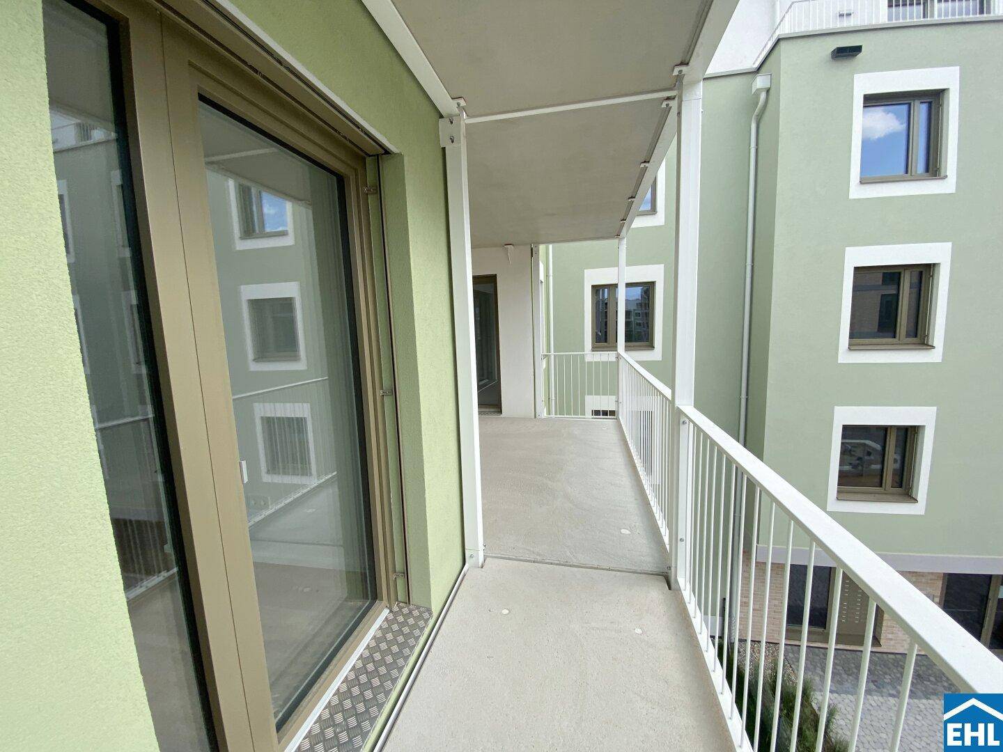 Langer Balkon entlang der Gebäudefassade mit Blick auf die benachbarten Wohnungen.