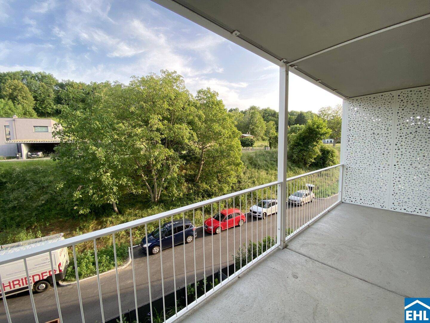 Geräumiger Balkon mit Metallgeländer und weitem Blick ins Grüne und auf die Straße.