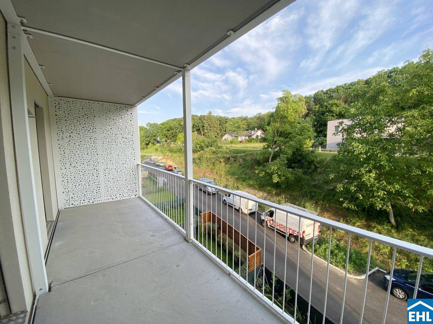 Heller Balkon mit schlichtem Design und Ausblick auf die bewaldete Umgebung.