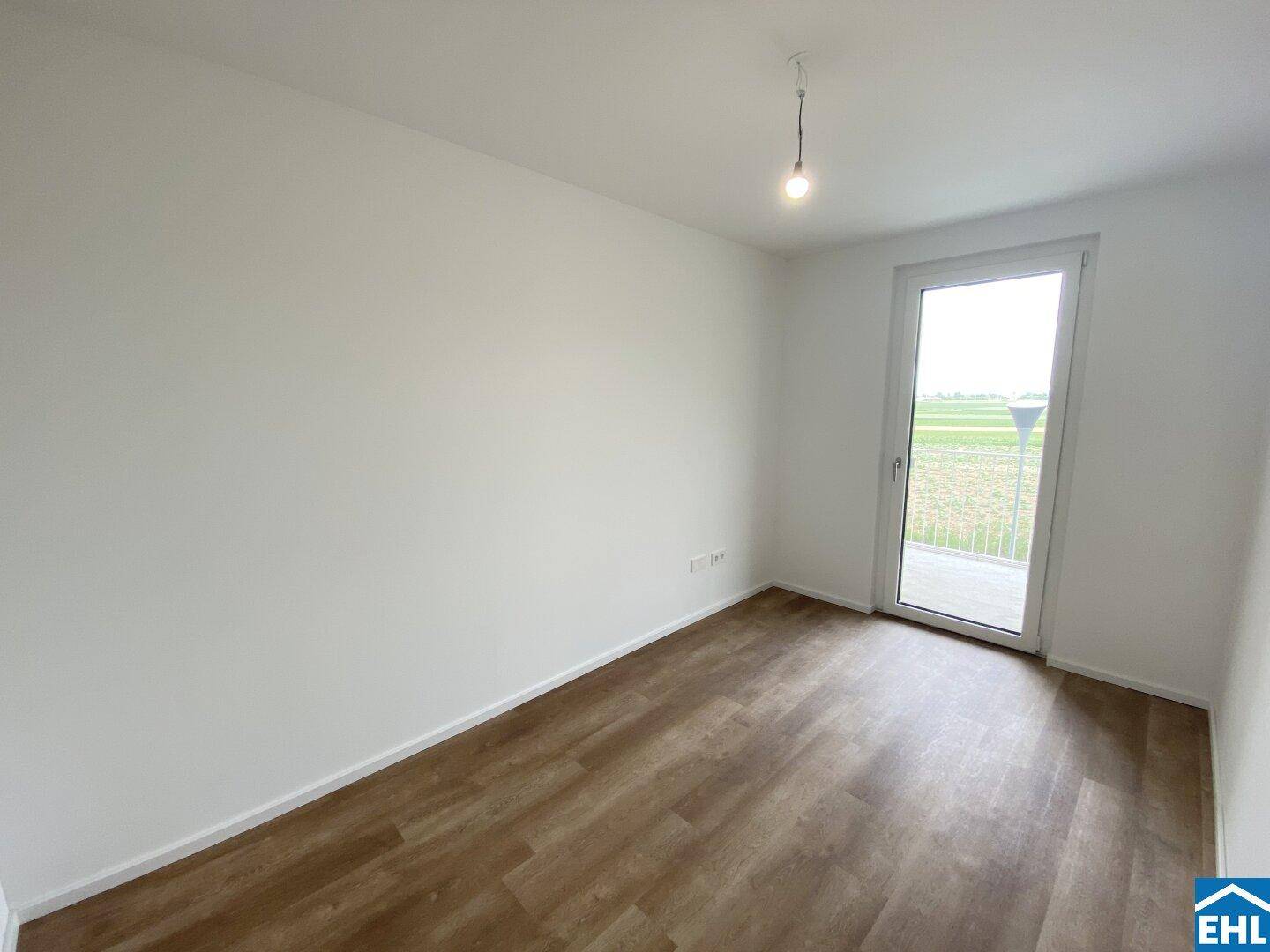 Helles Zimmer mit Vinylboden und großem Fenster, das Zugang zu einem Balkon mit freiem Blick bietet.