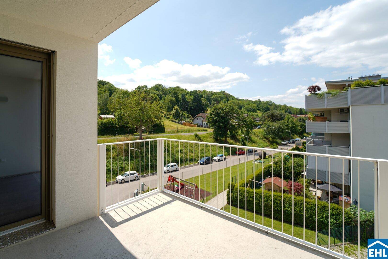 Sonniger Balkon mit Panoramablick auf die Umgebung, inklusive Spielplatz und weitere Gebäude.