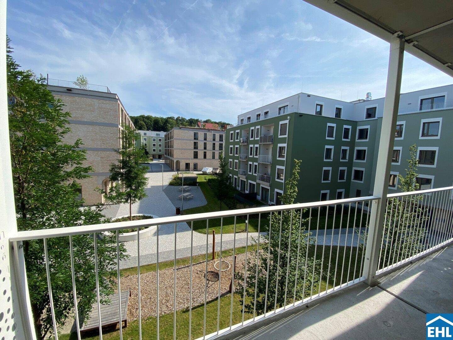 Balkon mit weitem Blick über den grünen Innenhof und die umliegende Wohnanlage.