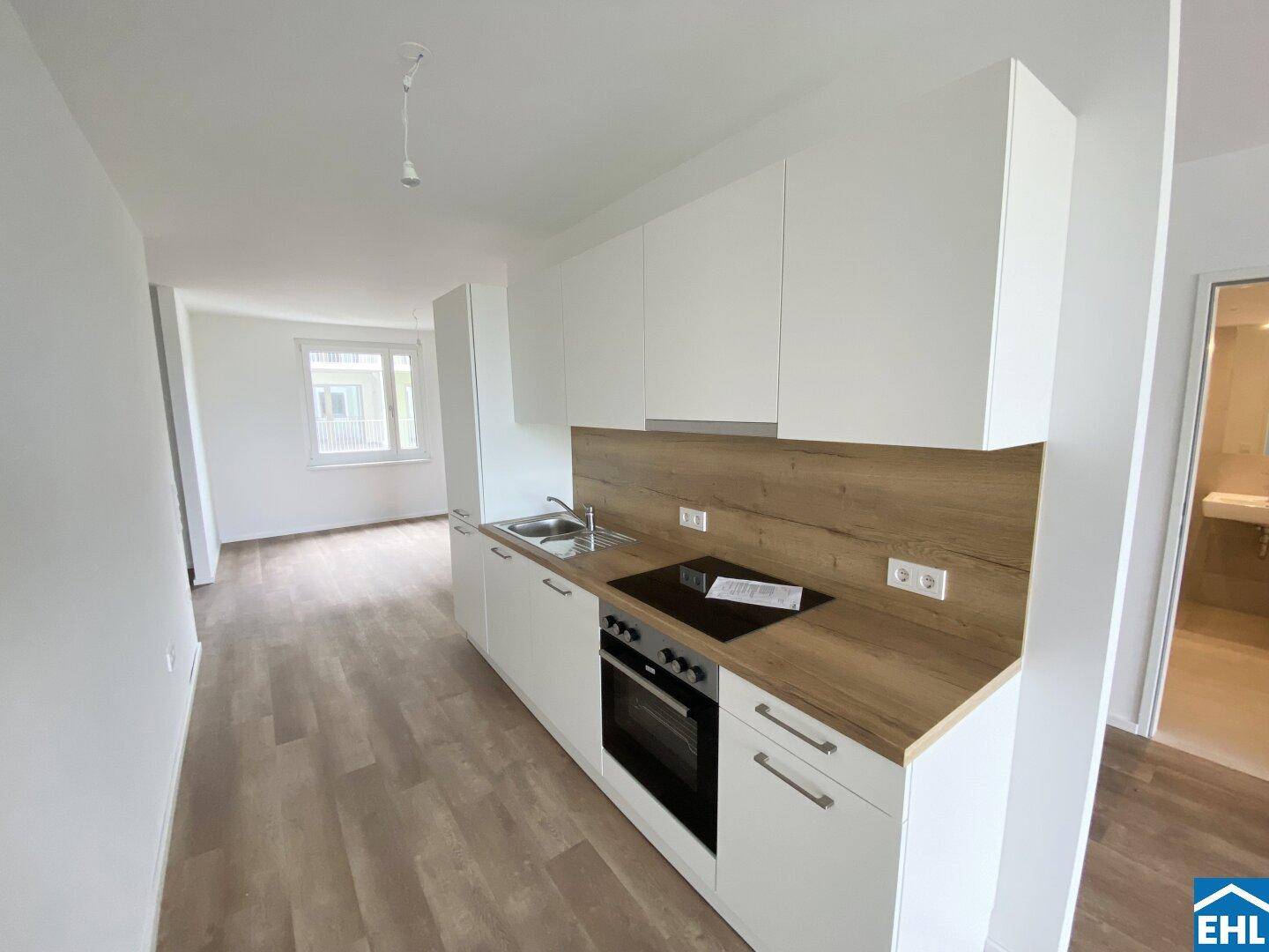 Moderne Einbauküche mit weißen Schränken, Holzoptik-Arbeitsplatte und integrierten Geräten in einem hellen Raum.